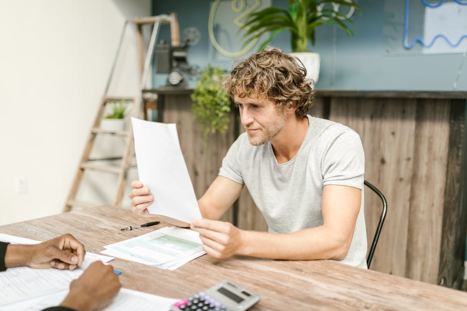A man with curly hair evaluates documents at a desk, highlighting focused work in a professional setting.
